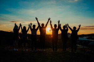 A group of people with their hands up in front of the setting sun